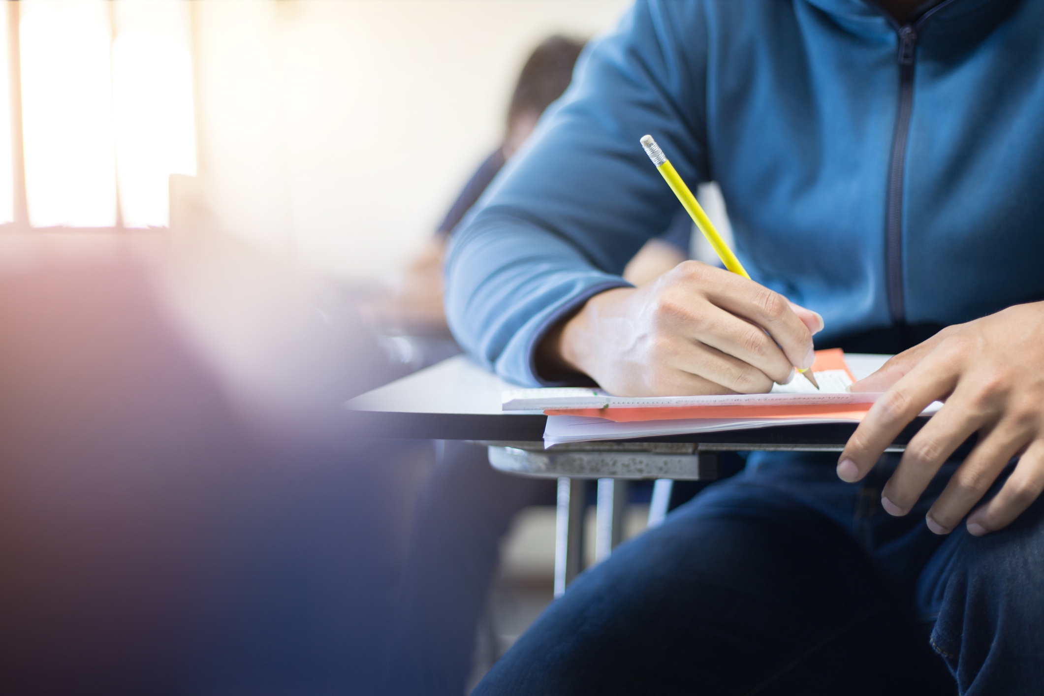 High schooler at desk writing with pencil